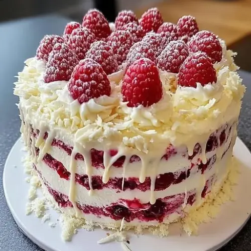 A slice of dreamy white chocolate raspberry cake with fresh raspberries on top.